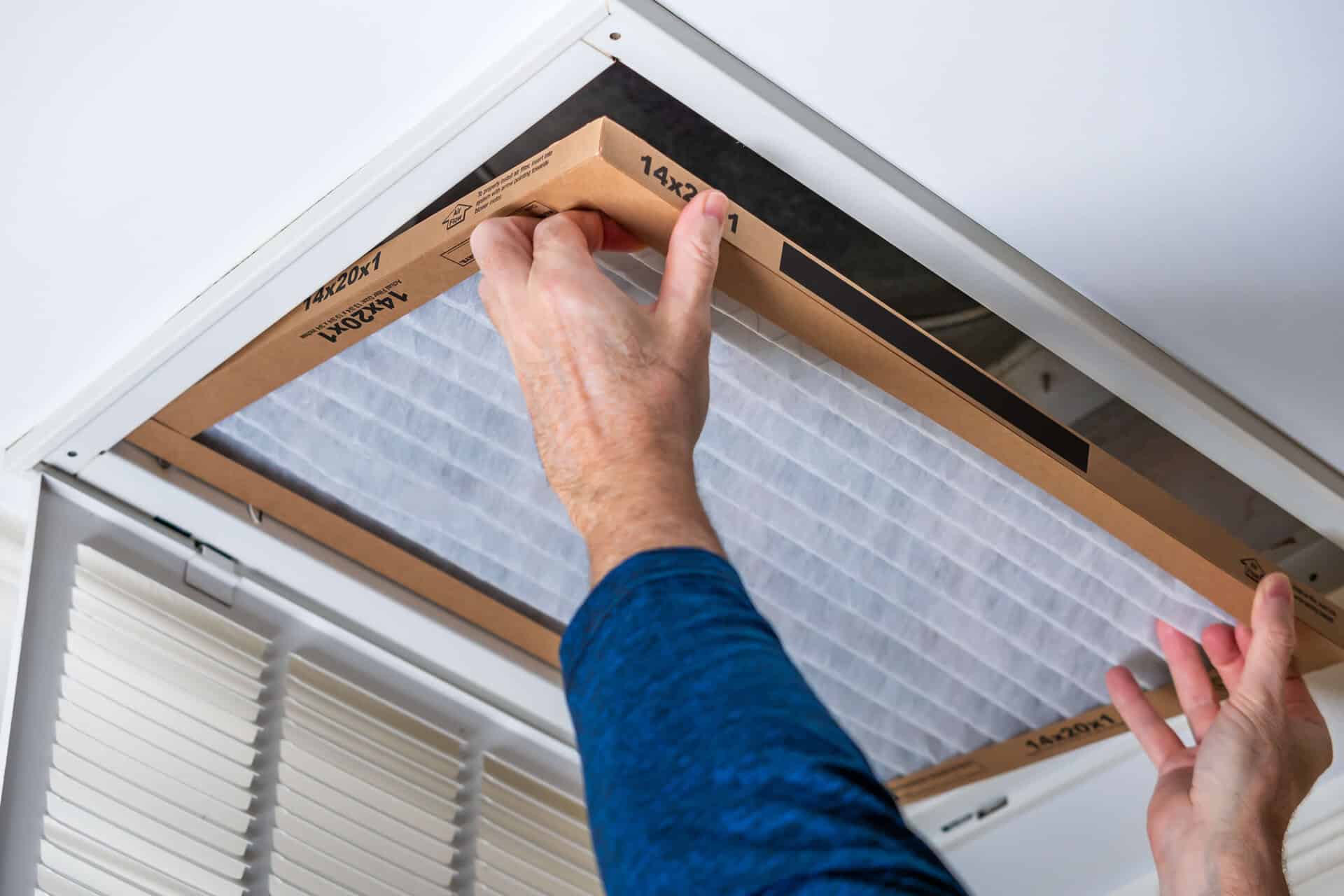 Man replacing dirty HVAC air filter in ceiling vent. Home air duct system maintenance for clean air